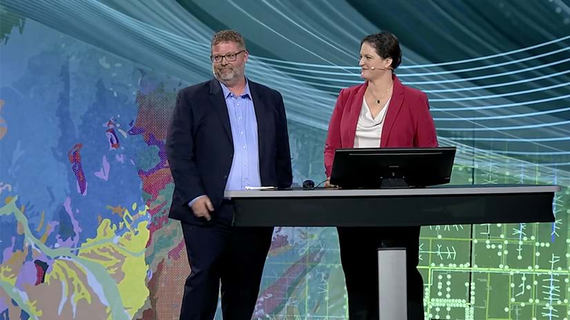 Two people standing in front of a desk on a conference presentation stage and smiling
