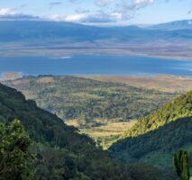 A landscape mountain view overlooking a green rangeland, lake, and mountains